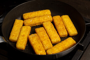 Fish sticks in a pan. Preparation of frozen fish sticks. Fast food.