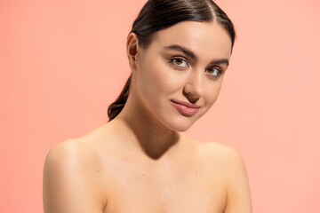 charming young woman with bare shoulders looking at camera isolated on pink.