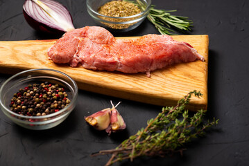 Raw meat steaks on a cutting board. Dark background. Preparation for cooking pork meat. Various spices, seasonings lie nearby.