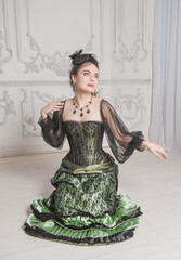 Beautiful woman wearing green medieval vintage Victorian Style dress sitting on the floor.