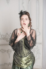 Astonished Beautiful woman wearing green medieval vintage Victorian Style dress holding hand near...