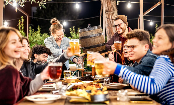 Young men and women having fun drinking out at beer garden patio - Social gathering and beverage life style concept on happy people enjoying weekend cookout time together at night - Vivid dark filter