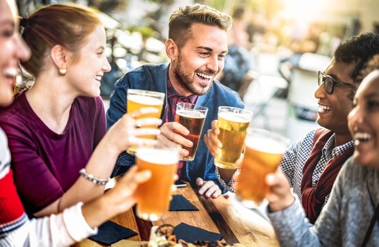 Young people drinking beer pints at brewery bar garden - Genuine beverage life style concept with guys and girls sharing happy hour together at open air pub dehor - Warm sunset backlight filter