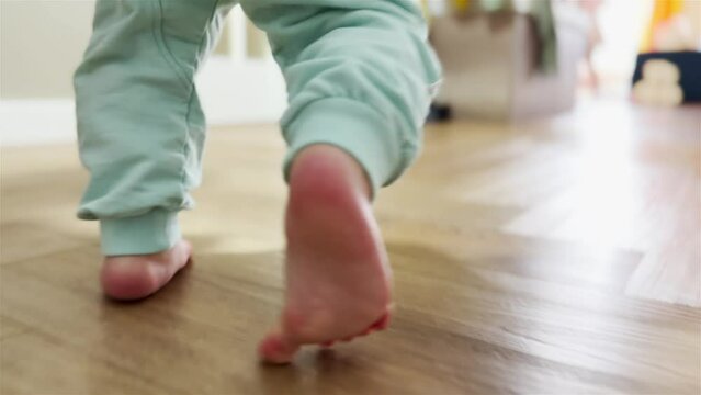 baby newborn first steps. mother teaches daughter baby to take the first steps with bare feet on the floor. baby walks barefoot on the floor at home light learning. baby newborn indoors first steps