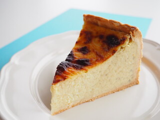 Slice of french custard tart (flan pâtissier) on white and blue background