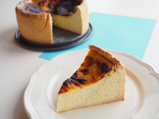 Slice of french custard tart (flan pâtissier) with the whole tart behind, white and blue background