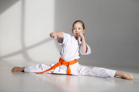 Karate training, a little girl in a kimono sits on a twine on a white background.