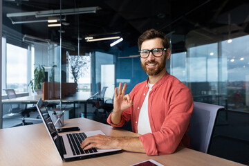 Portrait of a young male programmer, a freelancer who is reading in the office, sitting behind a...