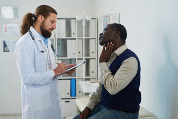 Obraz premium Mature male patient describing symptoms to endocrinologist making notes in document during medical consultation in clinics