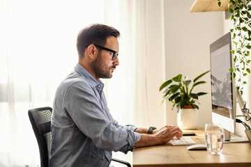 Focused creative writer is typing on computer while sitting at home office.