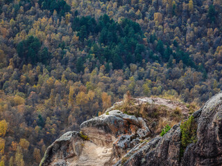 Minimalistic landscape of a rocky ledge against the background of a mountain forest. The edge of a stone cliff, a dangerous gorge.