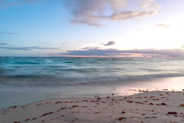Long exposure of a pastel colored sunset with tranquil turquoise waves washing up on a beach in...
