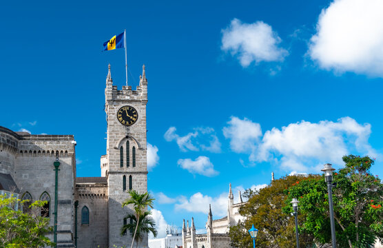 View of an historic building with a tower in Bridgetown, Barbados, West Indies with clock and flag and tree lined street.