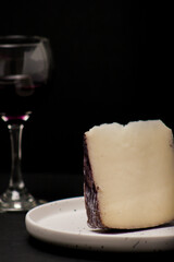 Close-up of a glass of wine on a black background next to a slice of wine cheese served on a white plate
