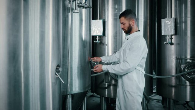 cylindrical-conical fermentation tanks with beer in modern brewery, man is taking sample