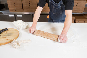 Dough for pizza, the chef rolls out the blanks. Closeup hand of chef baker in uniform white apron cook pizza at kitchen