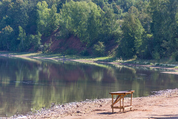 a wood table sitting on the shore of a lake, green forest on background