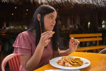 Caucasian latin dominican woman eating in restaurant shrimps with fried green plantain tostones.