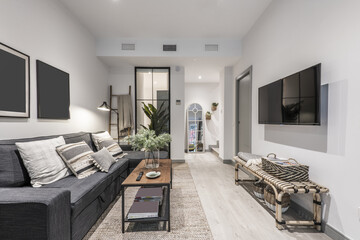 Living room of a house with a three-seater sofa with a chaise longue in gray fabric and a glass partition on one wall, an industrial-style coffee table and a TV hanging on the wall