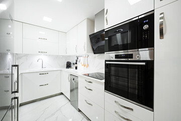 kitchen furnished with bright white furniture, smooth white countertops, white marble tiled floors and walls with veins and black glass and stainless steel appliances