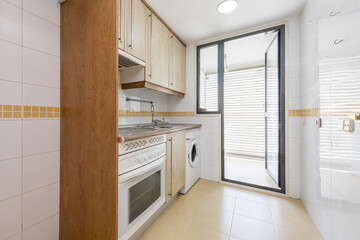Kitchen furnished on one side with light wood furniture, integrated white appliances and exit to a drying terrace with glass door and aluminum structure