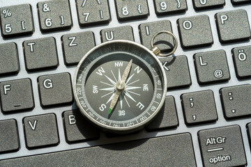 One single compass laying on a modern computer desktop PC keyboard, world navigation, different...