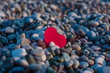 Obraz premium Red heart among sea pebbles.