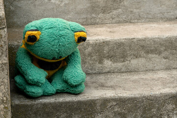 Sad depressed abandoned green frog plush toy plushie sitting on the stairs alone, feeling down,...