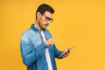 Concentrated on work. Confident young handsome man in casual working on laptop while standing against yellow background.