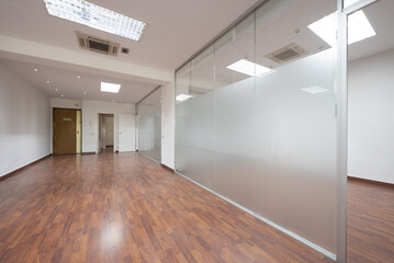 An empty office with dark wooden floors, technical ceilings and tempered glass dividing screens and...
