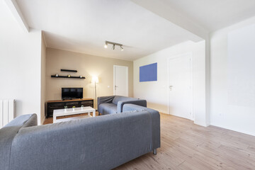 Vacation rental apartment with a living-dining room with chestnut wood floors, an industrial-style sideboard with a TV, gray fabric sofas, and a large window with an awning