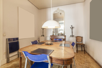 Dining room of a home with a vintage wooden table and blue plastic and metal folding chairs in a room with oak parquet floors