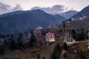 Fototapeta na wymiar aerial drone shot of manali hill station blue hour evening with building lights at dusk showing valley with fog covered himalaya mountains showing tourist spot in himachal