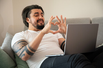 Handsome young man in front of laptop showing heart with hands