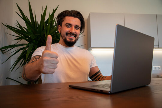 Handsome young man sitting in front of laptop showing thumbs up