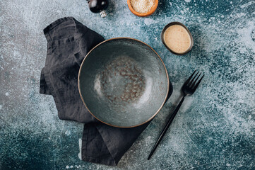 Empty black bowl with linen napkin, fork and sesame sauce over old gray background