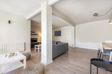 Living room of a holiday rental house with chestnut wood floors with natural fiber poufs, gray fabric sofas and a white square coffee table