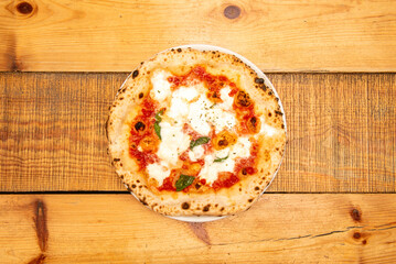 The most typical, simple and famous Italian stone-baked margherita pizza on a wooden table