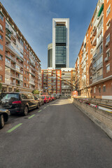 Fototapeta premium Street with parked cars, residential buildings on all sides and towers of the Madrid skyline in the background