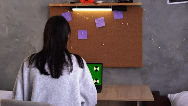 Serious female college student studying in dormitory using laptop computer with green mock up display, chroma key display. Copy space