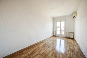 Empty room with oak parquet with glossy varnish, aluminum radiators and balcony with folding doors