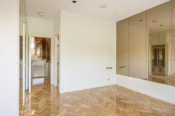 Empty room of an apartment with oak parquet with glossy varnish, a wall with mirror panels and built-in wardrobes with mirror doors