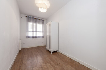 Empty room in an apartment with a matte wooden floor, a small white cabinet and a window with curtains
