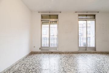 Empty room with terrazzo floors with black dots and two balconies with aluminum windows with sliding doors and old shutters