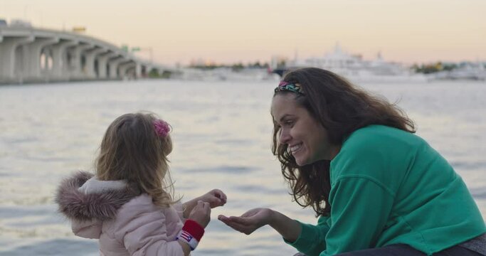 Mother and little daughter sitting by the water throwing rocks to water