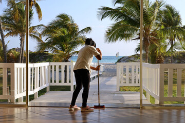 Black cleaning lady mops the floor at the entrance to the hotel from the sandy beach. View of the...