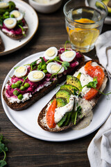 Two smorrebrods (open sandwiches with different toppings: avocado-salmon-cream cheese and quail eggs -beetroot - cream cheese) and glass of lemonade  on wooden table.