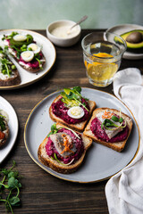 Mix of smorrebrods (open sandwiches) with different toppings: avocado-salmon-cream cheese, herring-beetroot paste, green peas - cottage cheese, quail eggs -beetroot - cream cheese; and mustard sauce 