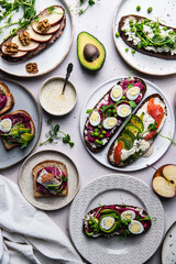 Mix of homemade smorrebrods (open sandwiches) with different toppings: avocado-salmon-cream cheese, herring-beetroot paste, green peas-cottage cheese, quail eggs -beetroot-cream cheese.