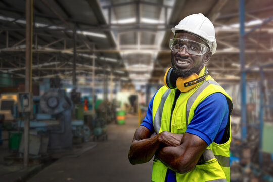 Portrait of manuel African black man worker is standing with confidence with blue working suite dress and safety helmet in front machine and equipment for heavy industry factory. Steel plant.